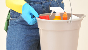 A person wearing jeans and holding cleaning supplies